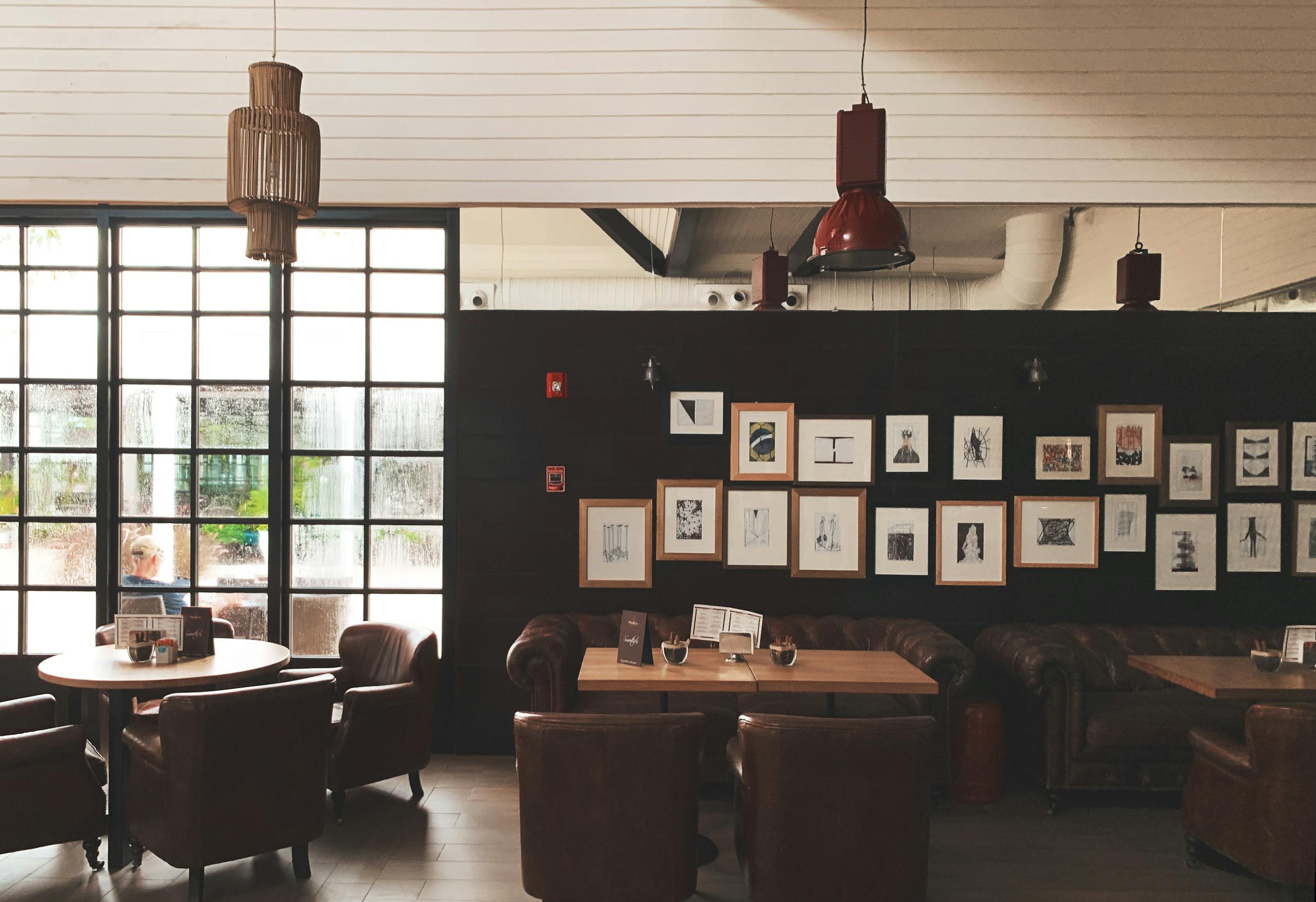 Cozy café interior featuring leather chairs, framed wall art, and pendant lighting. Ideal for meetings.